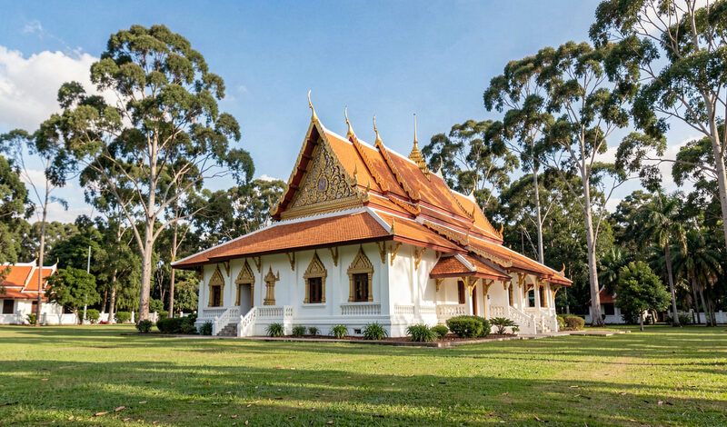 A white and gold temple building with tiered roofs among green lawns and tall Queensland trees.