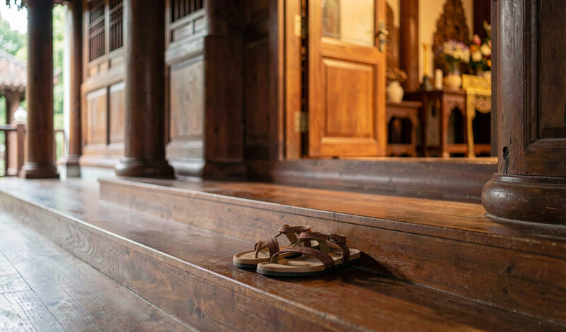 A pair of sandals left at the steps of a temple hall with polished timber floor and soft light inside.